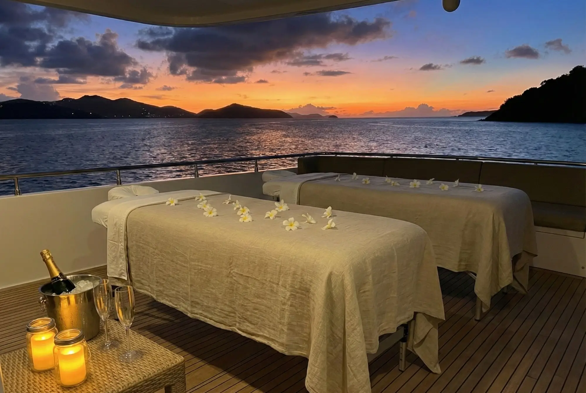 Romantic duo massage setup for couples on a private yacht deck at sunset in Saint Martin, featuring champagne and tropical flowers.