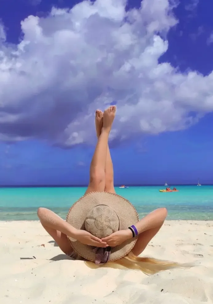 A woman relaxing on the white sand of a St Maarten beach, illustrating the abrasive reality of an outdoor beach massage compared to the pristine, sand-free comfort of a bespoke in-villa spa ritual in SXM.